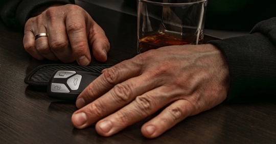 driver's hand, glass of alcohol, and car keys