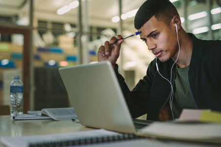 male-student-sitting-at-laptop-with-headphones-in